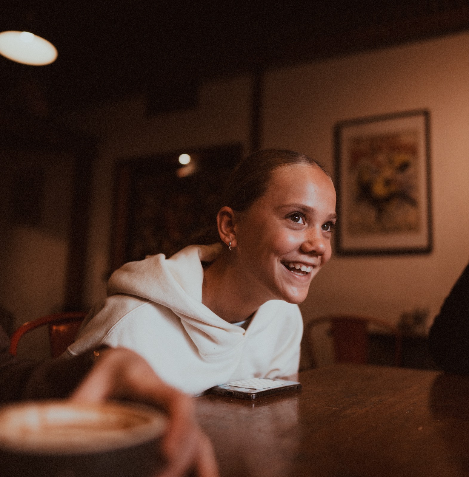 Girl laughing across a café table, warm documentary tones