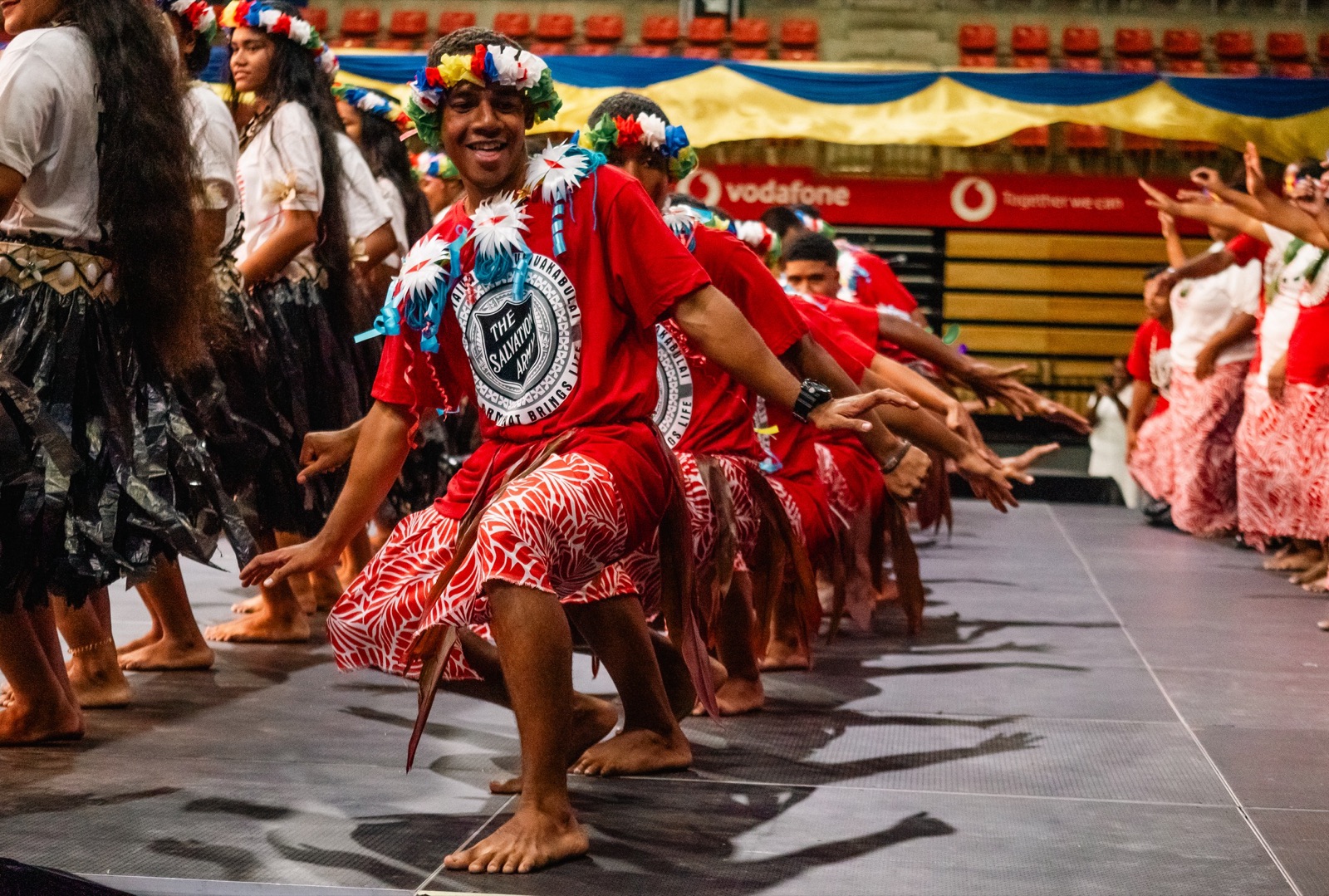 Pasifika dancers in red mid-performance on an arena floor