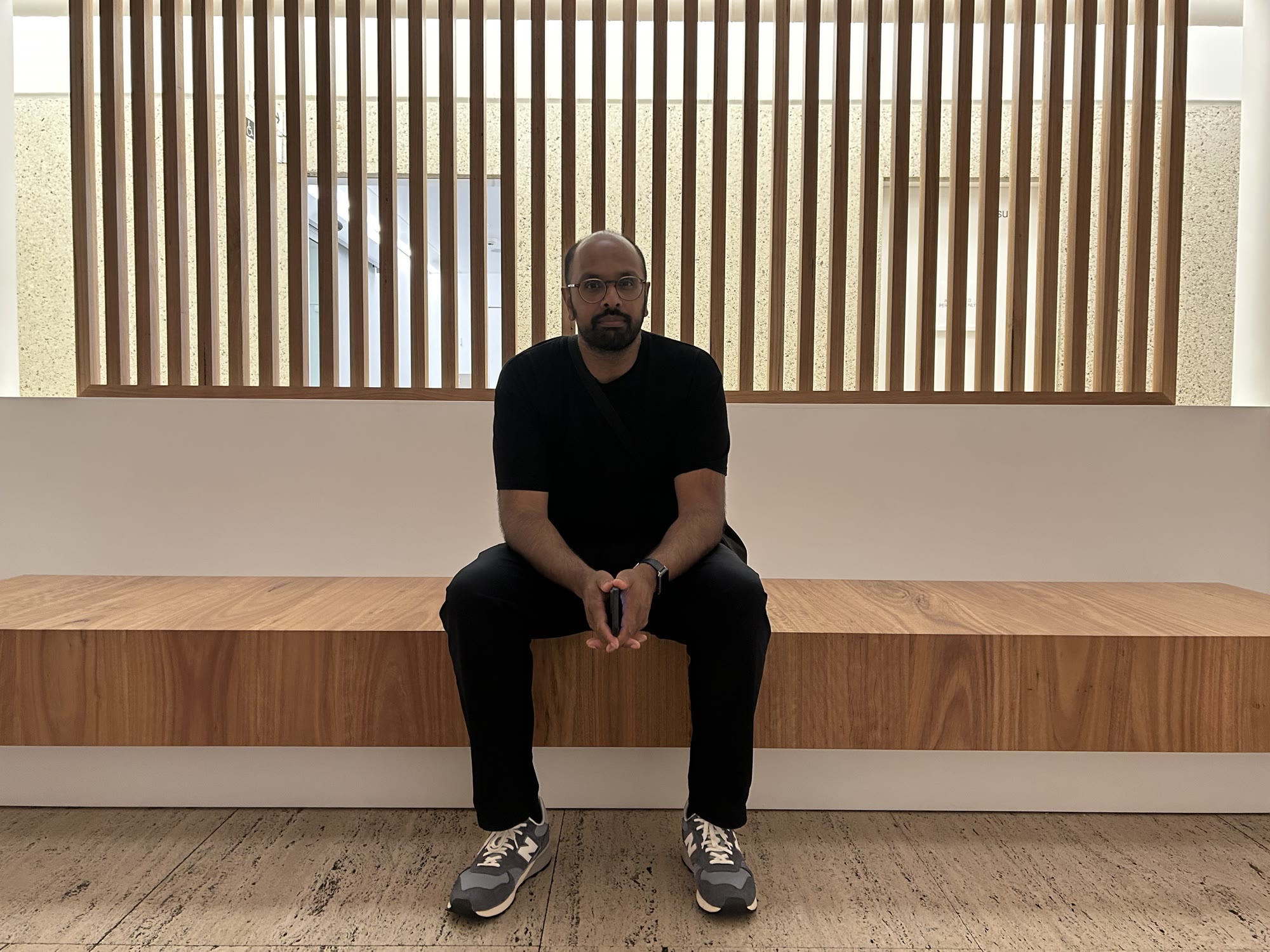 Kris Singh seated on a long timber bench against a slatted screen